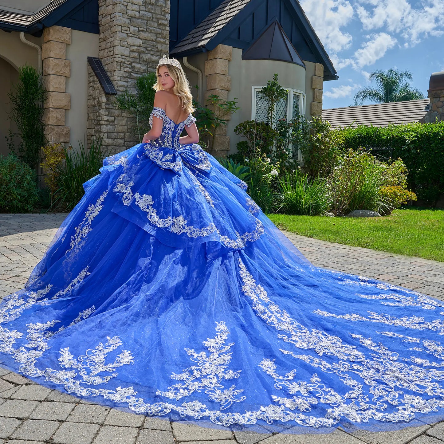 Front zoom view of a woman wearing royal blue quinceañera dress with white lace detailing tiara sequin fringe ruffles