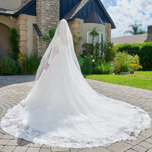 White wedding dress with a long train on a stone driveway in front of a house.