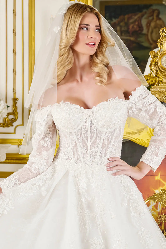 Woman wearing a white lace wedding dress with long sleeves in an ornate room.