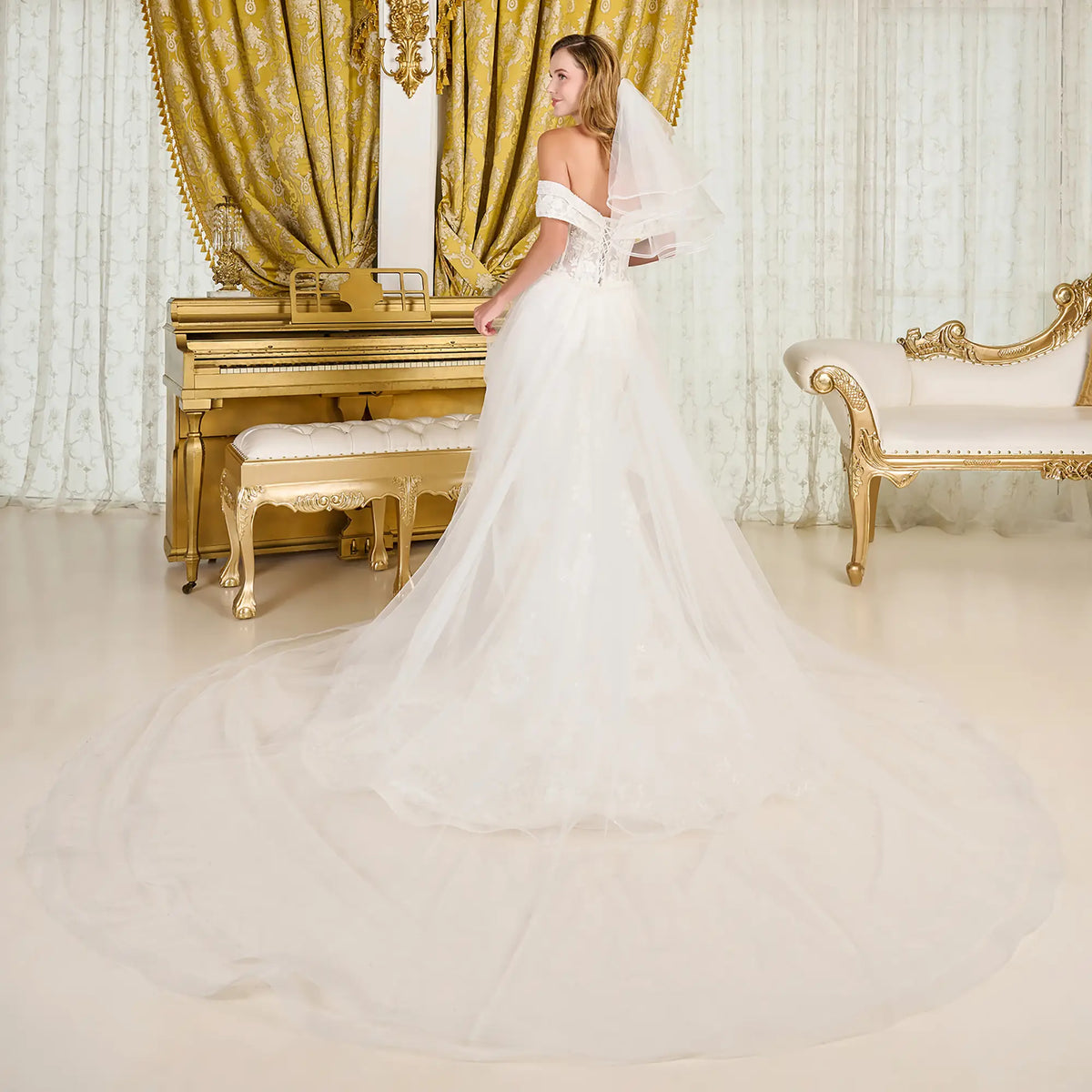 Woman in a white wedding dress standing in a opulent room with gold curtains and piano.