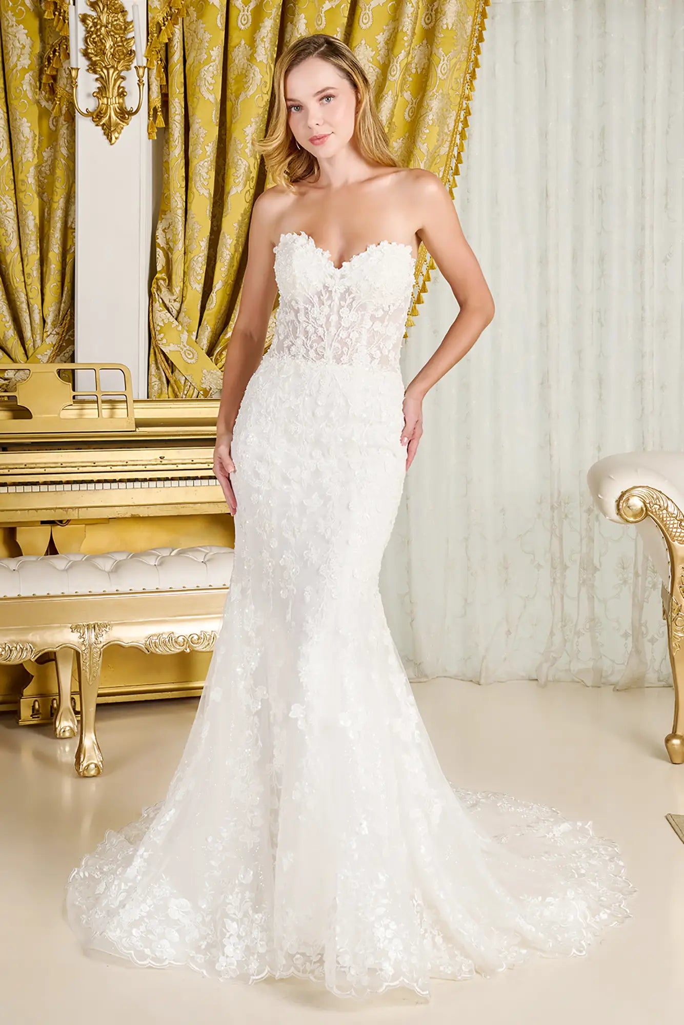 Woman in a white wedding dress standing in an opulent room with gold decor.