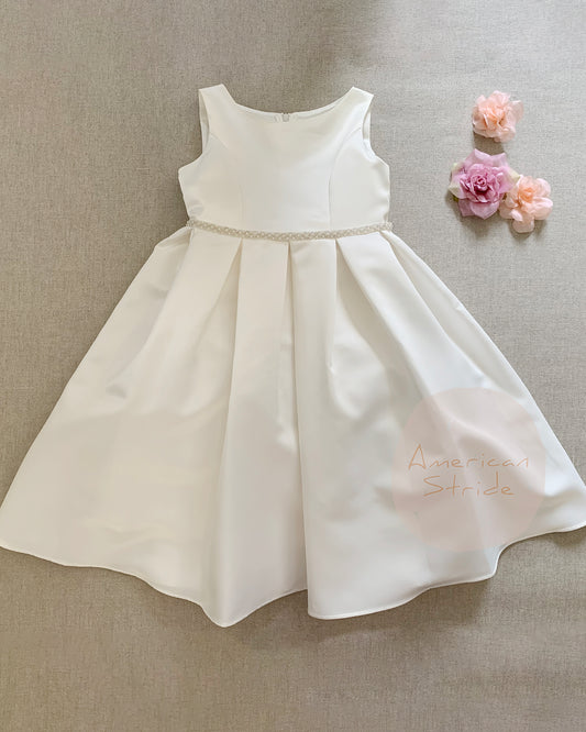 Ivory flower girl dress on a beige surface with pink flowers.