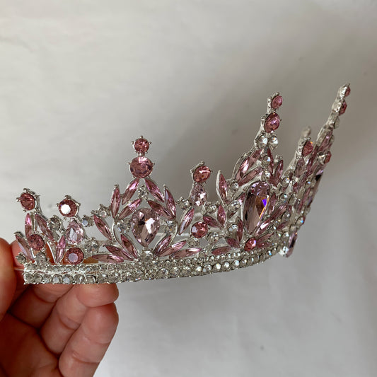 Pink and silver tiara held by a hand against a plain background
