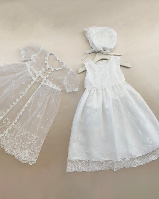 White baby baptism tulle dress with matching bonnet on a beige background