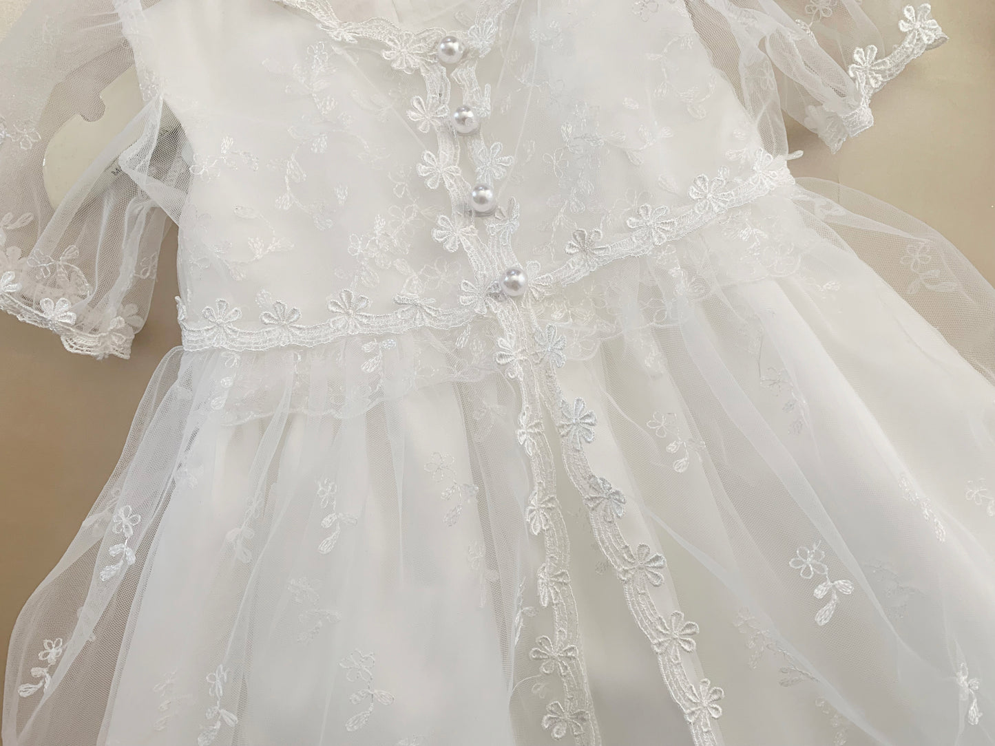 White baby baptism tulle dress with floral embroidery on a plain background