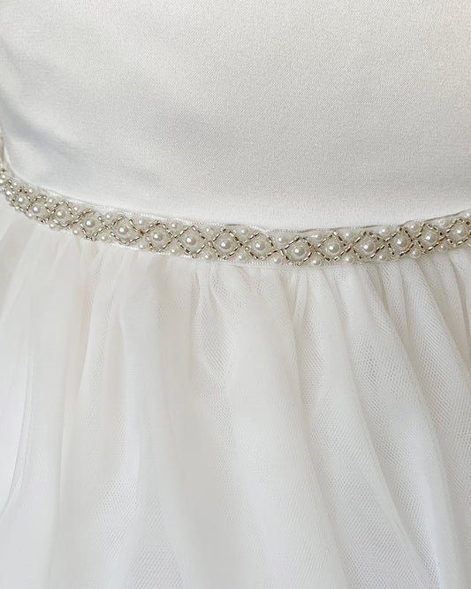 Close-up of an off white dress with a decorative ivory belt featuring pearls and crystals.