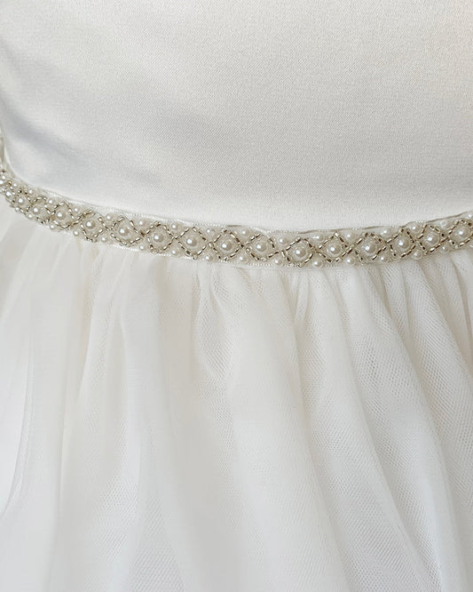 Close-up of an off white dress with a decorative ivory belt featuring pearls and crystals.