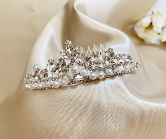 Silver tiara with pearls on a beige fabric background