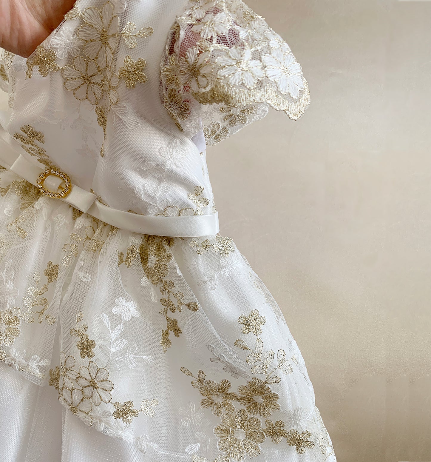 White lace dress with gold embroidery on a beige background