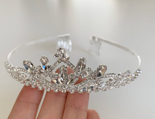 Silver tiara held by a hand against a white background