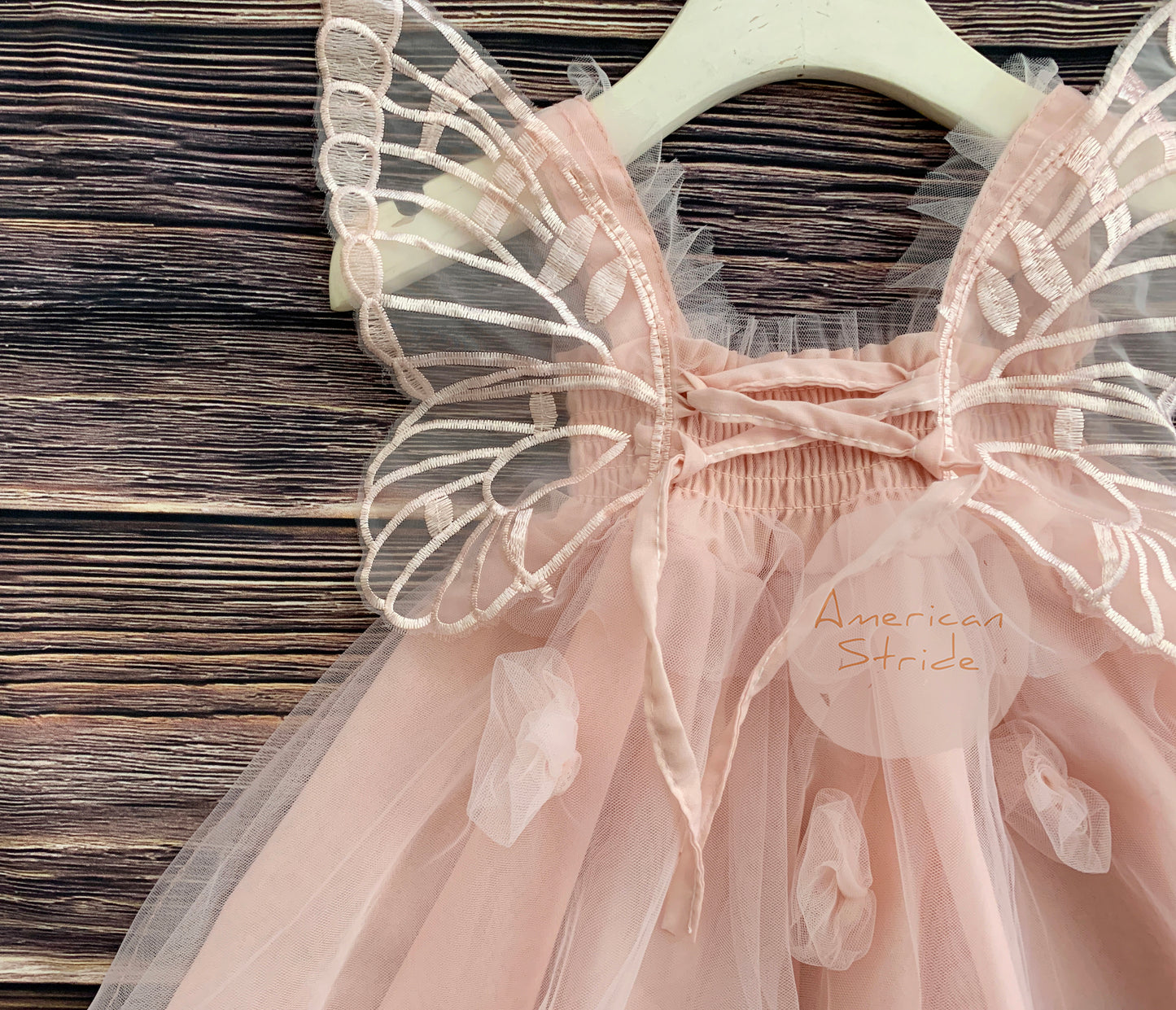 Pink fairy dress with butterfly wings on a wooden surface, brand 'American Stride' visible.