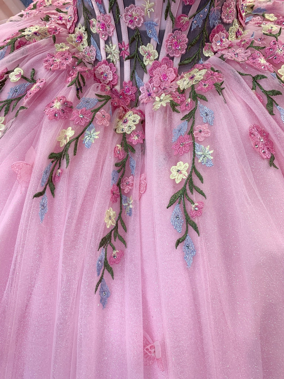 Detailed view highlights Pink quinceanera dress with pink tulle fabric with multicolor floral embroidery, sequins.