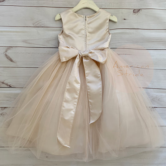 champagne rose flower girl dress with a bow on a wooden background