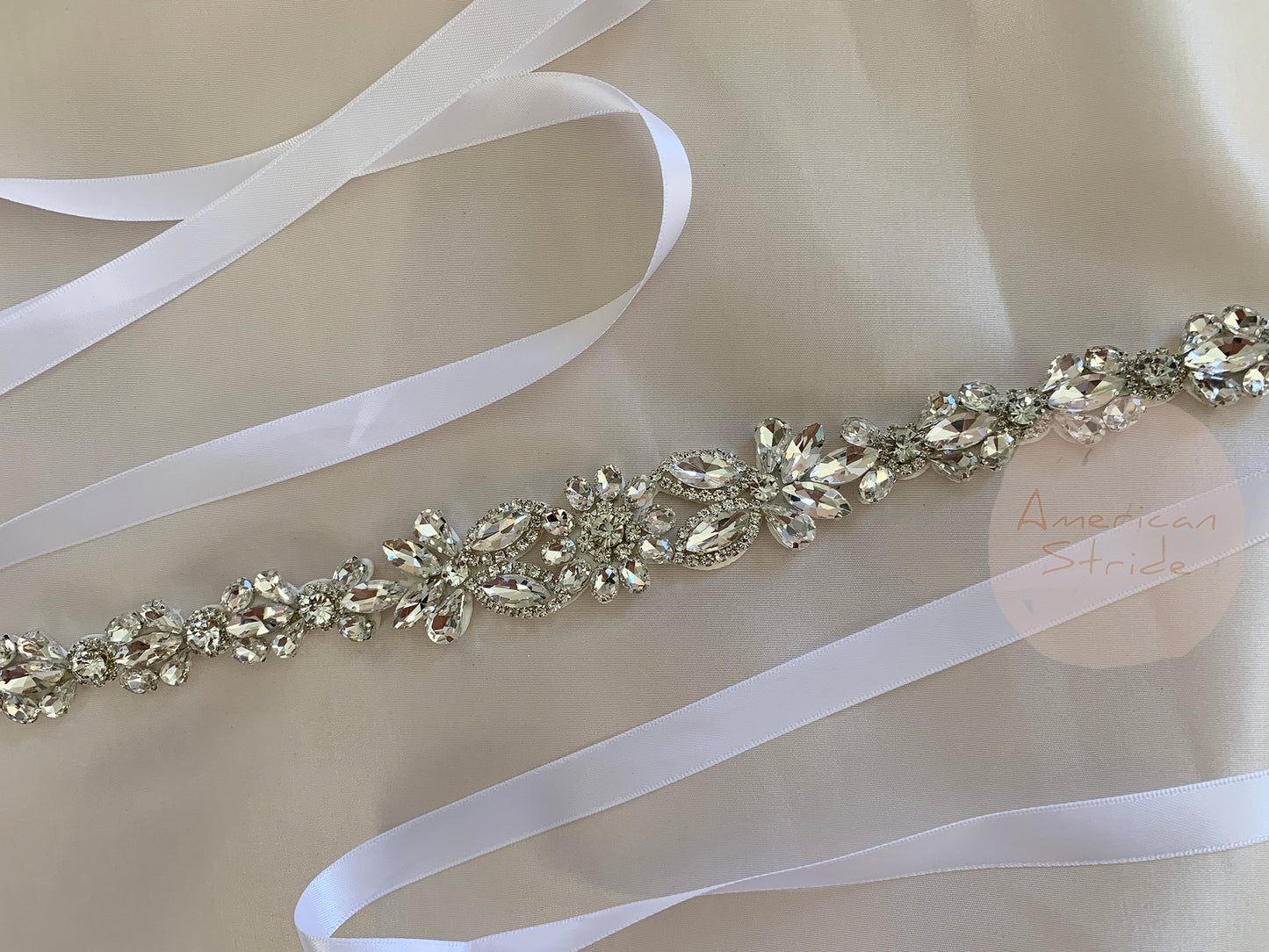 Silver rhinestone belt with white ribbon on a beige background