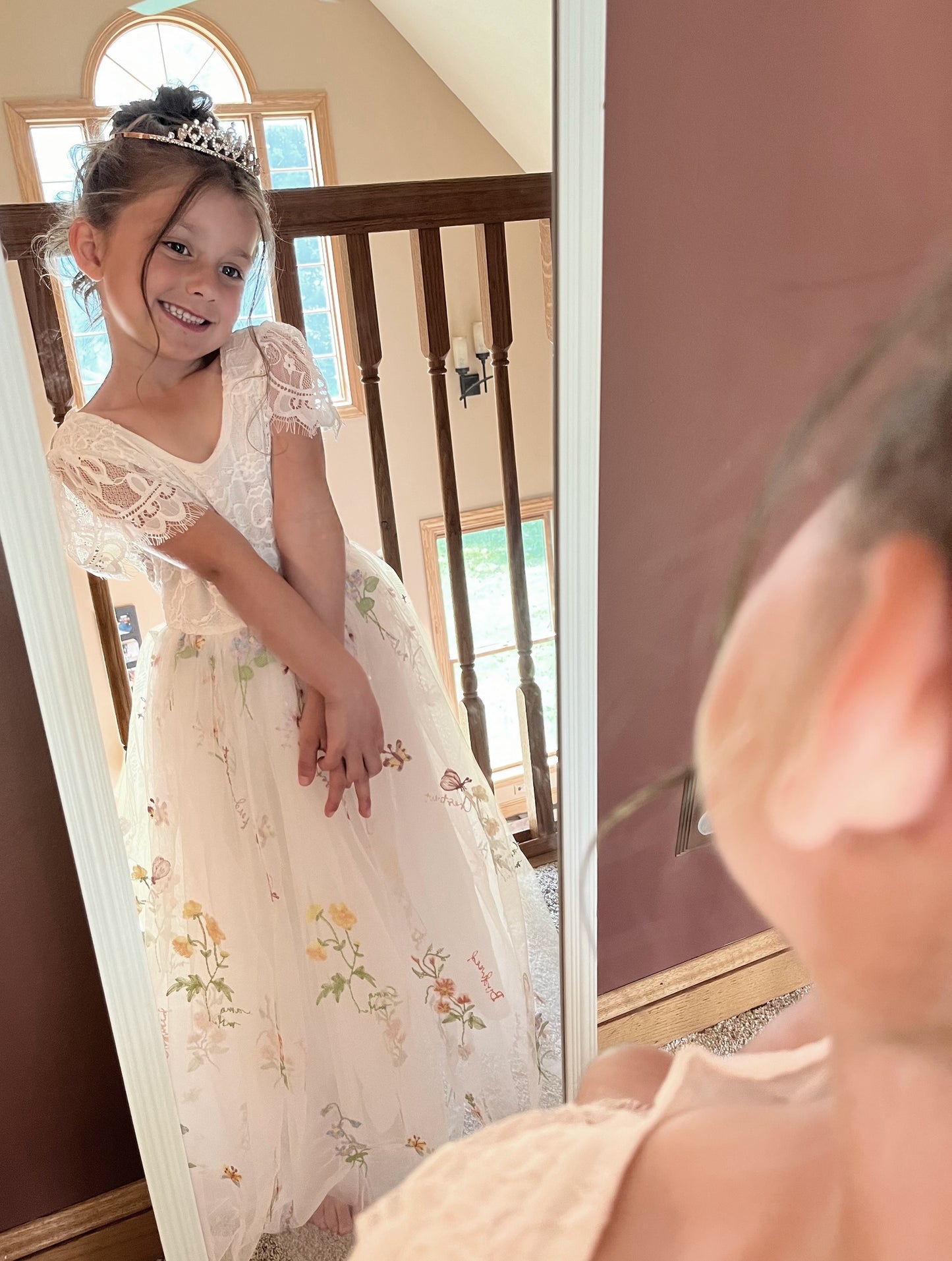 Young girl in a floral dress standing in front of a mirror.
