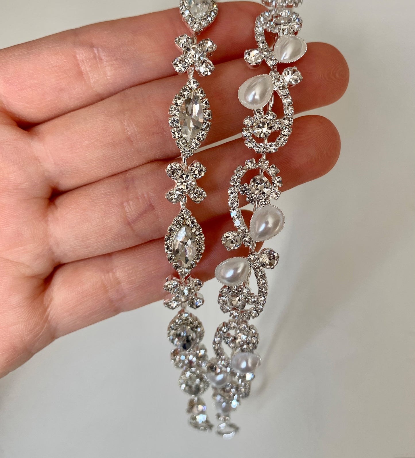 Silver jewelry piece held by a hand on a plain background