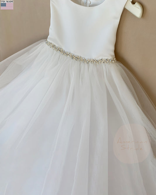 White flower girl dress with a beaded waistband on a beige background