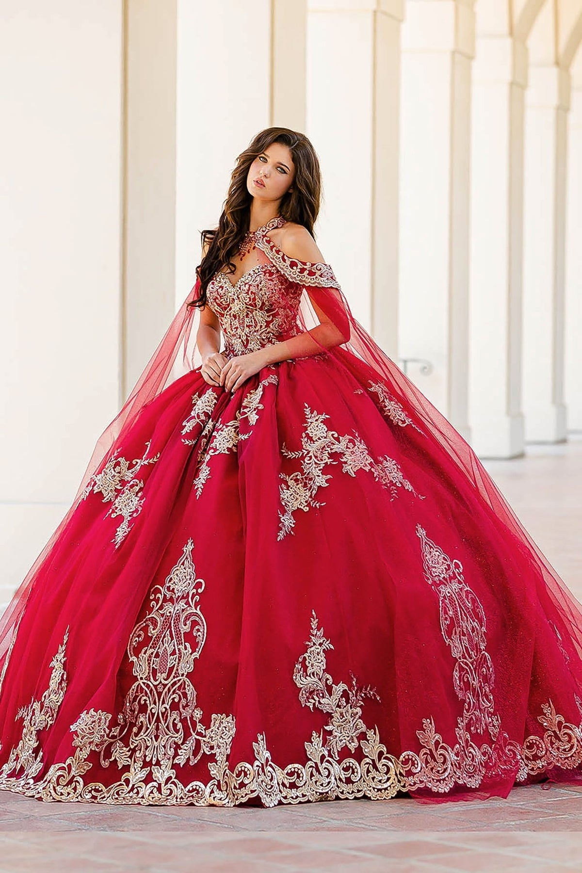 Hemline view highlights three-quarter a wine quinceañera dress with gold embroidery, cape and tulle skirt.
