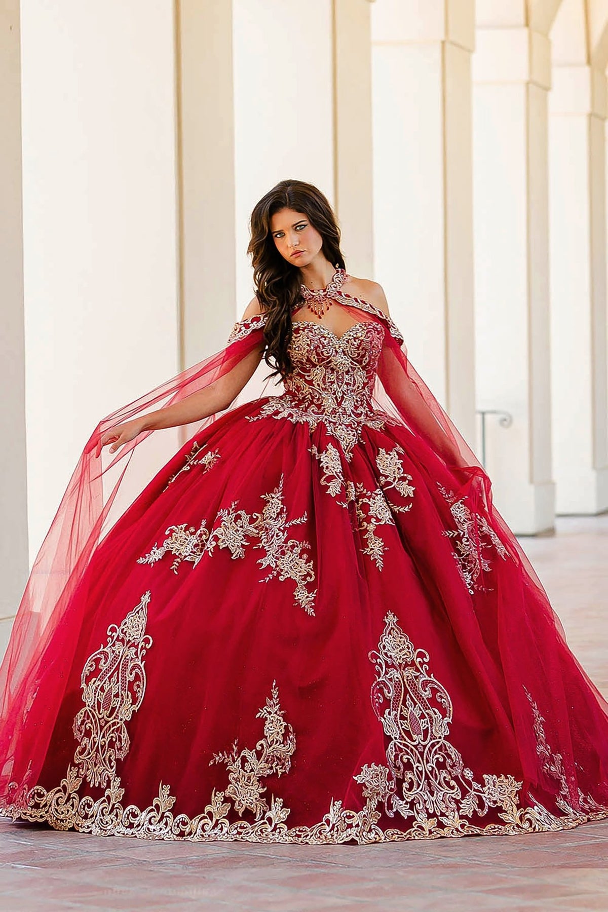 Train detail reveals a wine quinceañera dress with gold embroidery, lace applique, cape and tulle skirt.