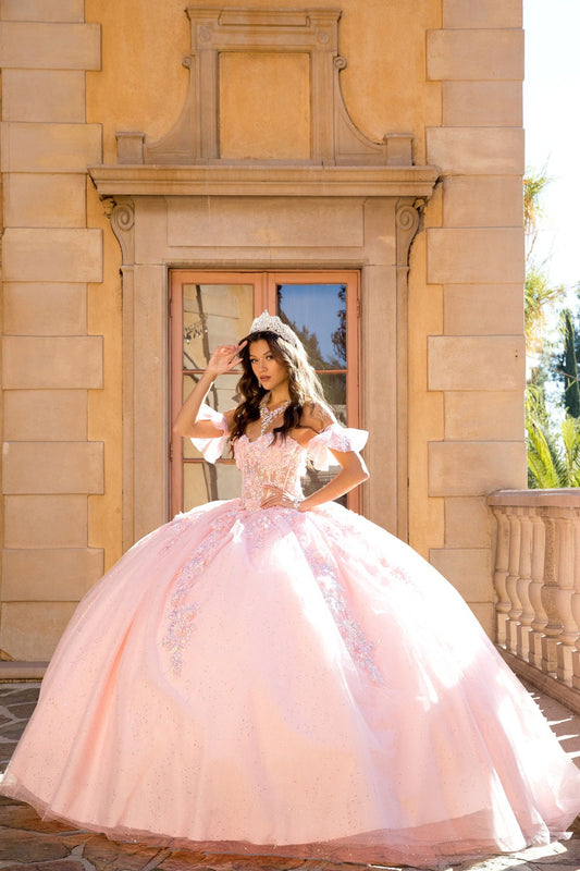 Full view of a woman wearing a blush quinceañera ball gown with sweetheart neckline, corset bodice, detachable sleeves and tulle skirt