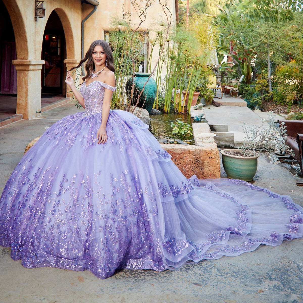 Intricate features stand out across a lilac quinceañera ball gown with ruffled train, gemstone embellishments and corset bodice.