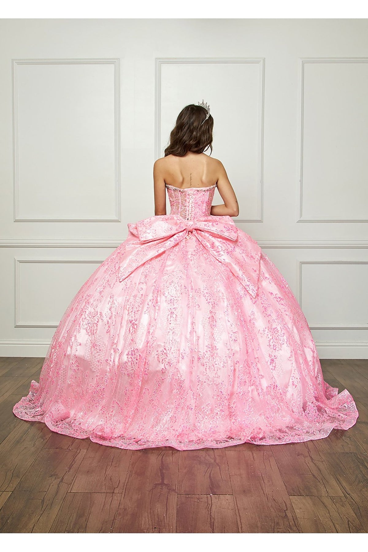 Rear view reveals a pink quinceañera ball gown with sparkling sequins, corset back, crown and large bow detail.