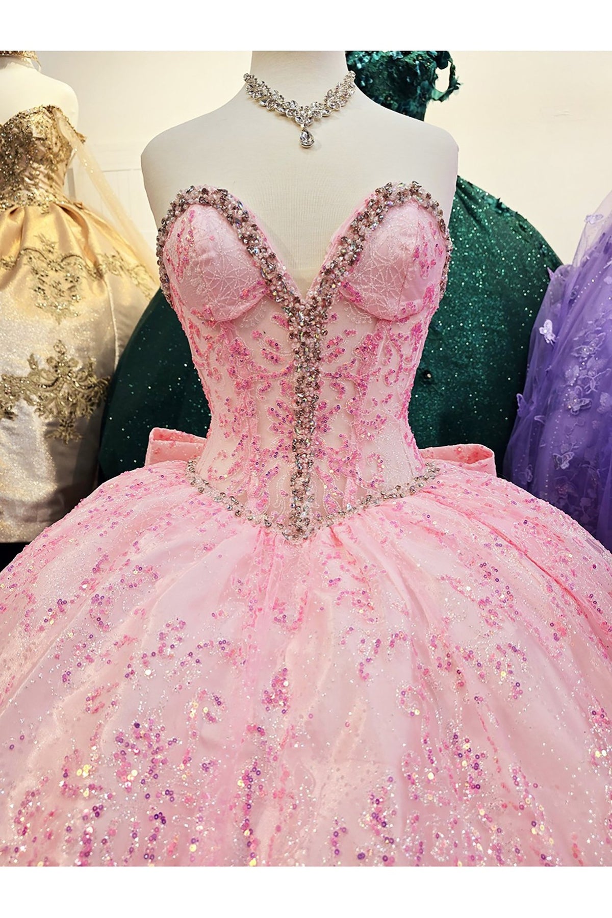 Close-up view reveals pink quinceañera ball gown with see-through corset bodice, lace details and sequin embellishments.