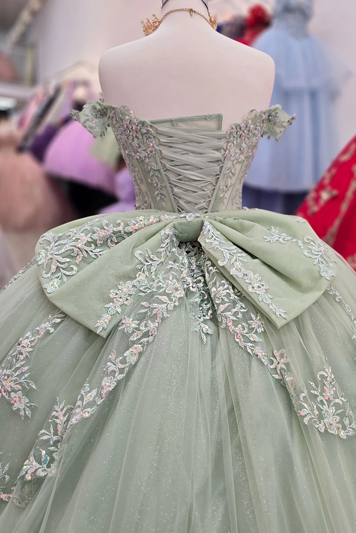 Rear view reveals sage green ball gown with floral embroidery and corset bodice displayed on a mannequin.