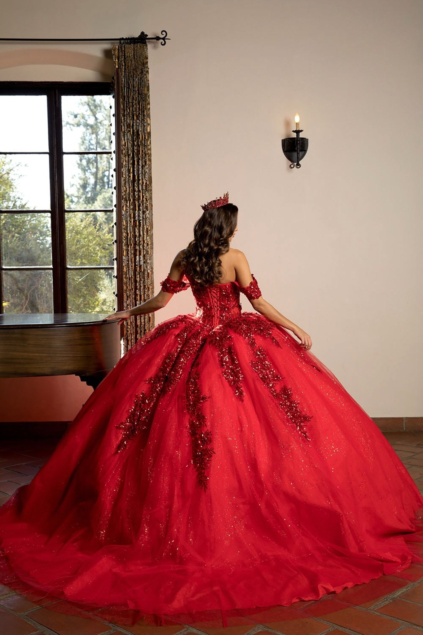 Back view of a woman wearing a red quinceañera ball gown with corset back, 3D flowers and glitter details