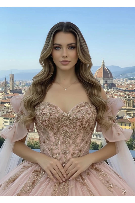 Close up Woman with long blonde hair wearing a Rose Gold off-the-shoulder ball gown with intricate floral embroidery, standing on a stone balcony overlooking a lush green vineyard under a clear blue sky.