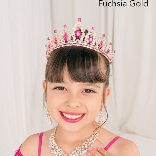 Young girl in a pink dress with a fuchsia gold tiara and necklace, against a plain background.