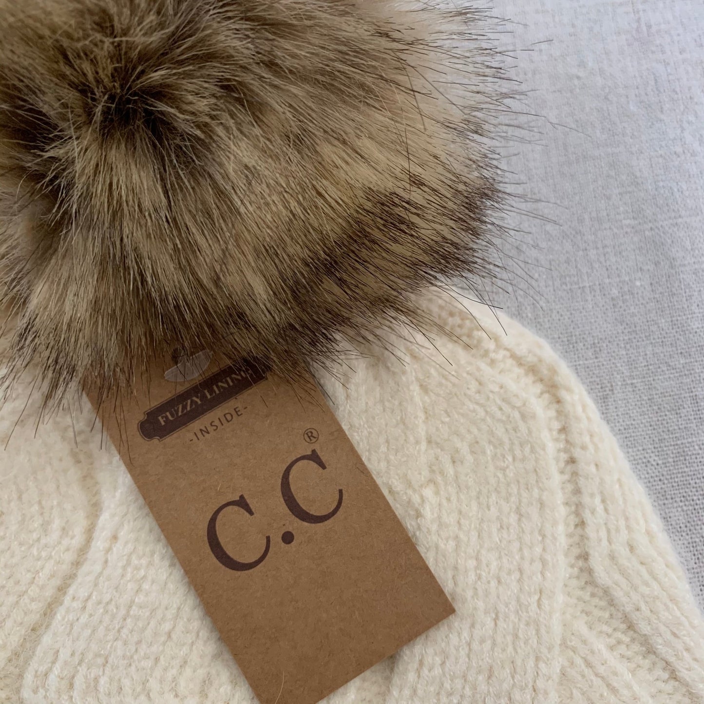 Ivory pom-pom women's winter beanie, close-up view, interior detail.