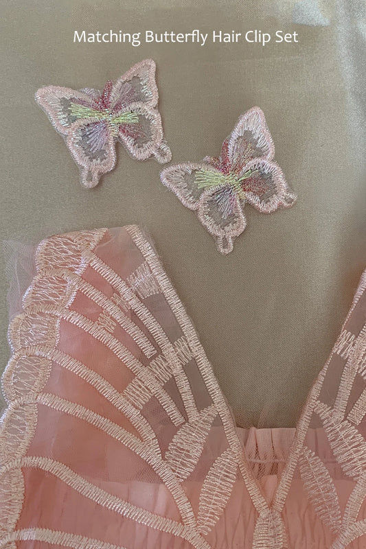 A close-up of a pale pink embroidered butterfly hair clip set placed on a soft beige fabric background