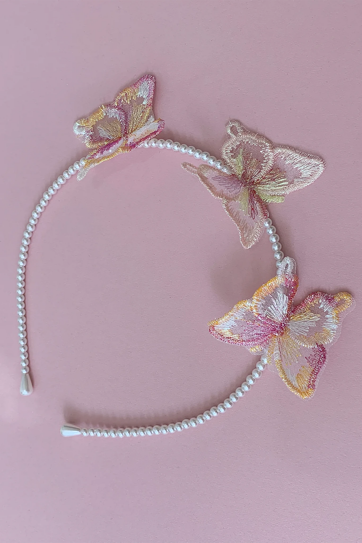 A white beaded headband decorated with three embroidered iridescent butterflies in pink, yellow, and beige