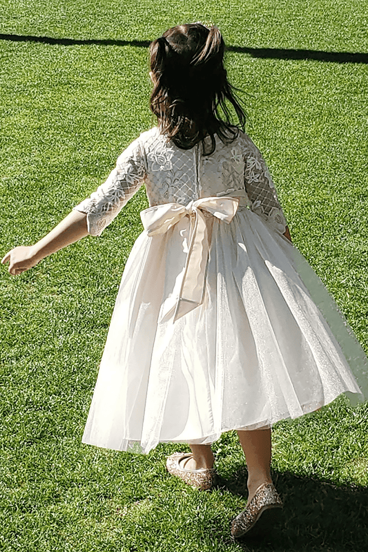 Child in a champagne dress with a large bow standing on grass