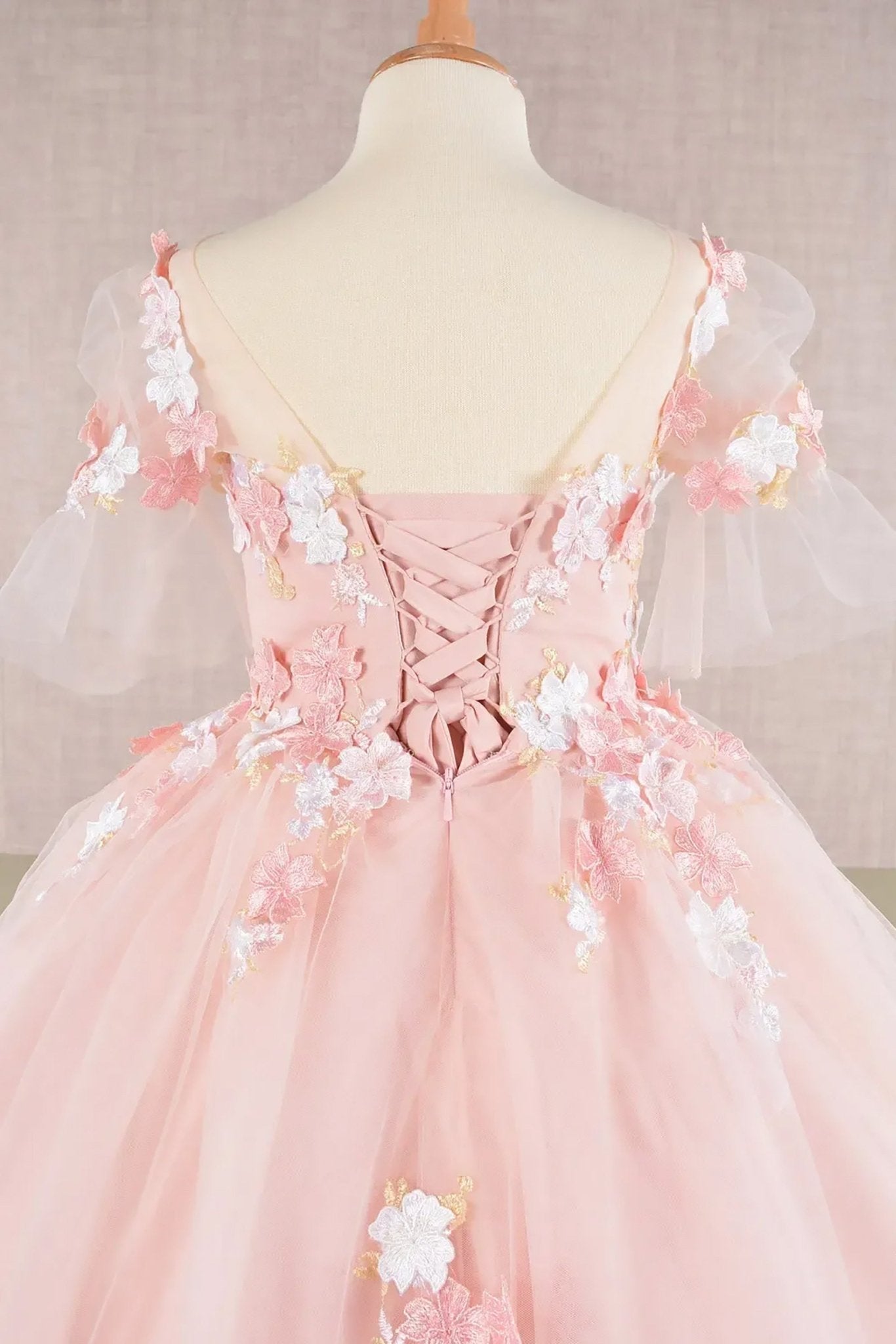 Back zoom view of a blush kid ballgown with 3D floral applique, puff sleeves, and lace back up