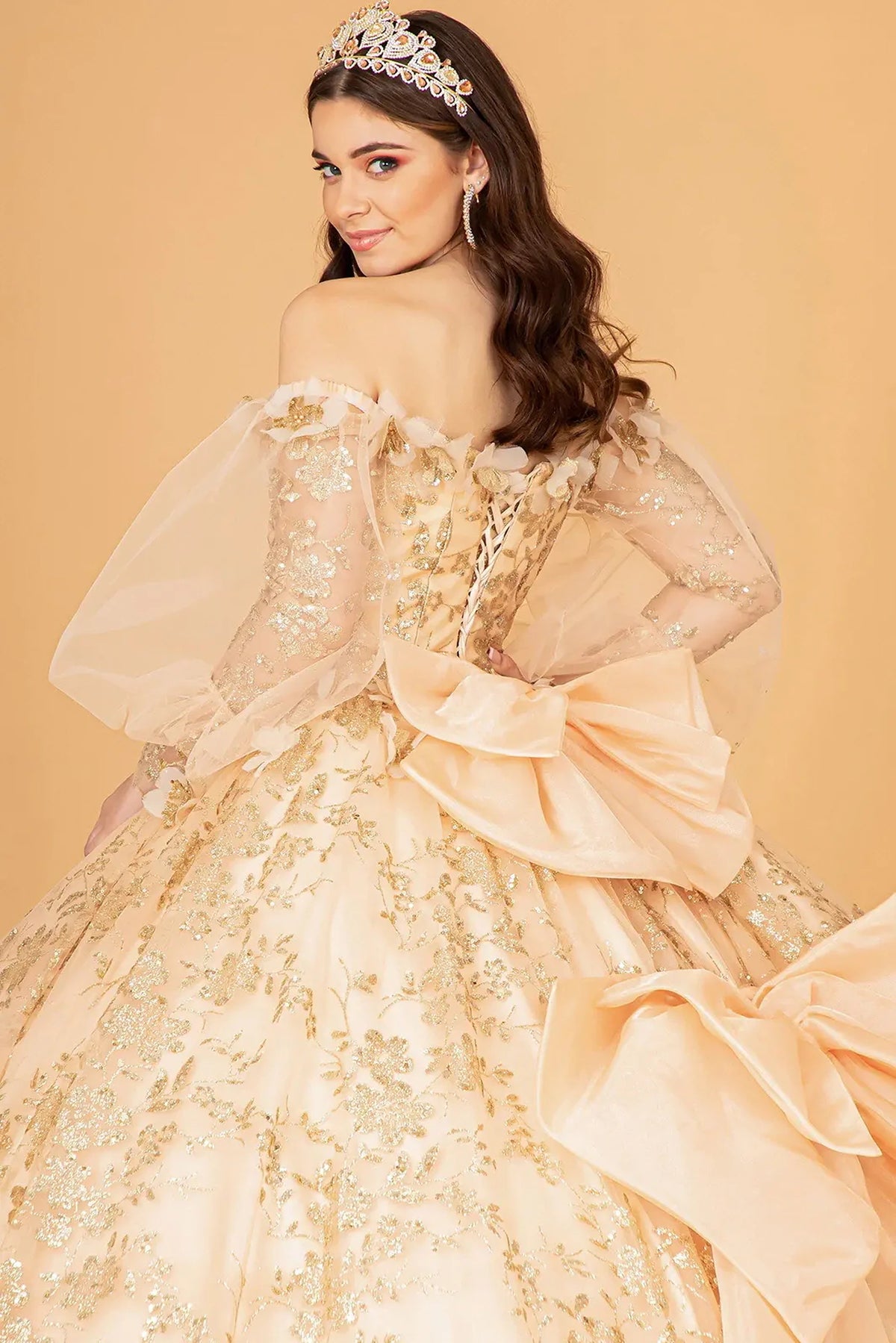 Layered skirt showcases the Gold quinceañera ball gown with detachable back bow.