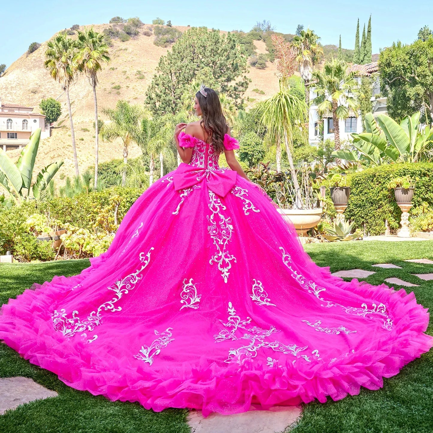 Back view of a woman wearing fuchsia quinceañera dress with intricate floral embroidery puff sleeves corset bodice ball gown