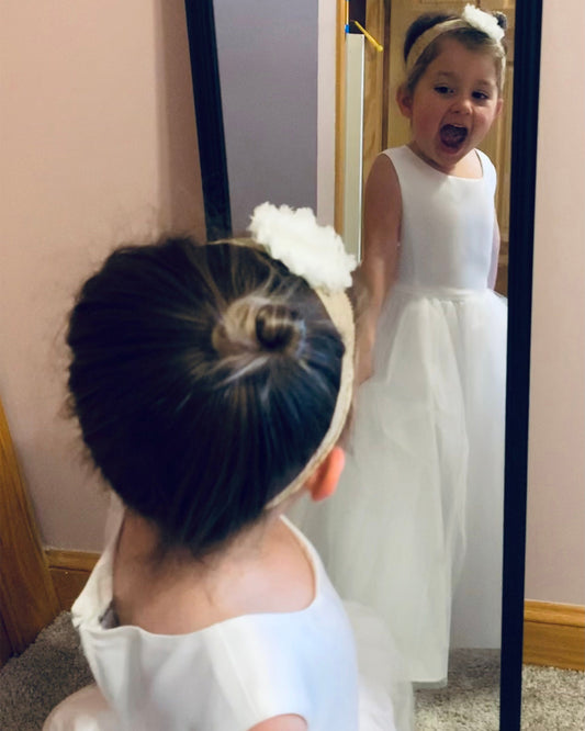 Child in a white dress looking at themselves in a mirror