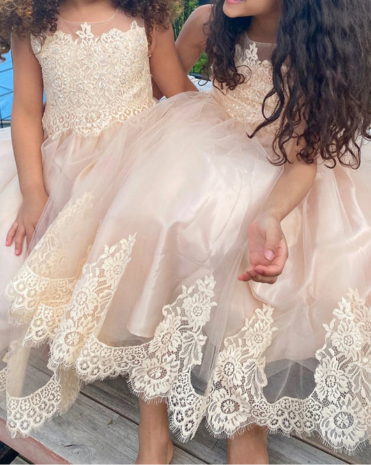 Two children wearing champagne lace dresses with a blurred background
