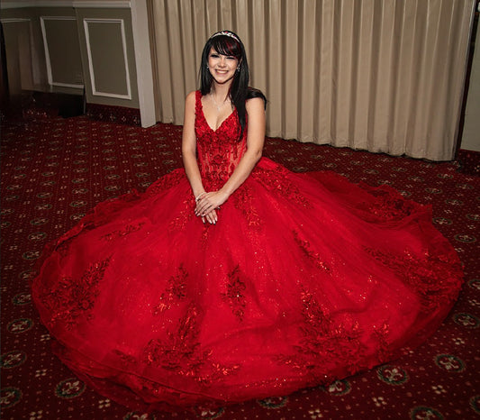 Woman with necklace and earring in a red gown sitting on a patterned carpet