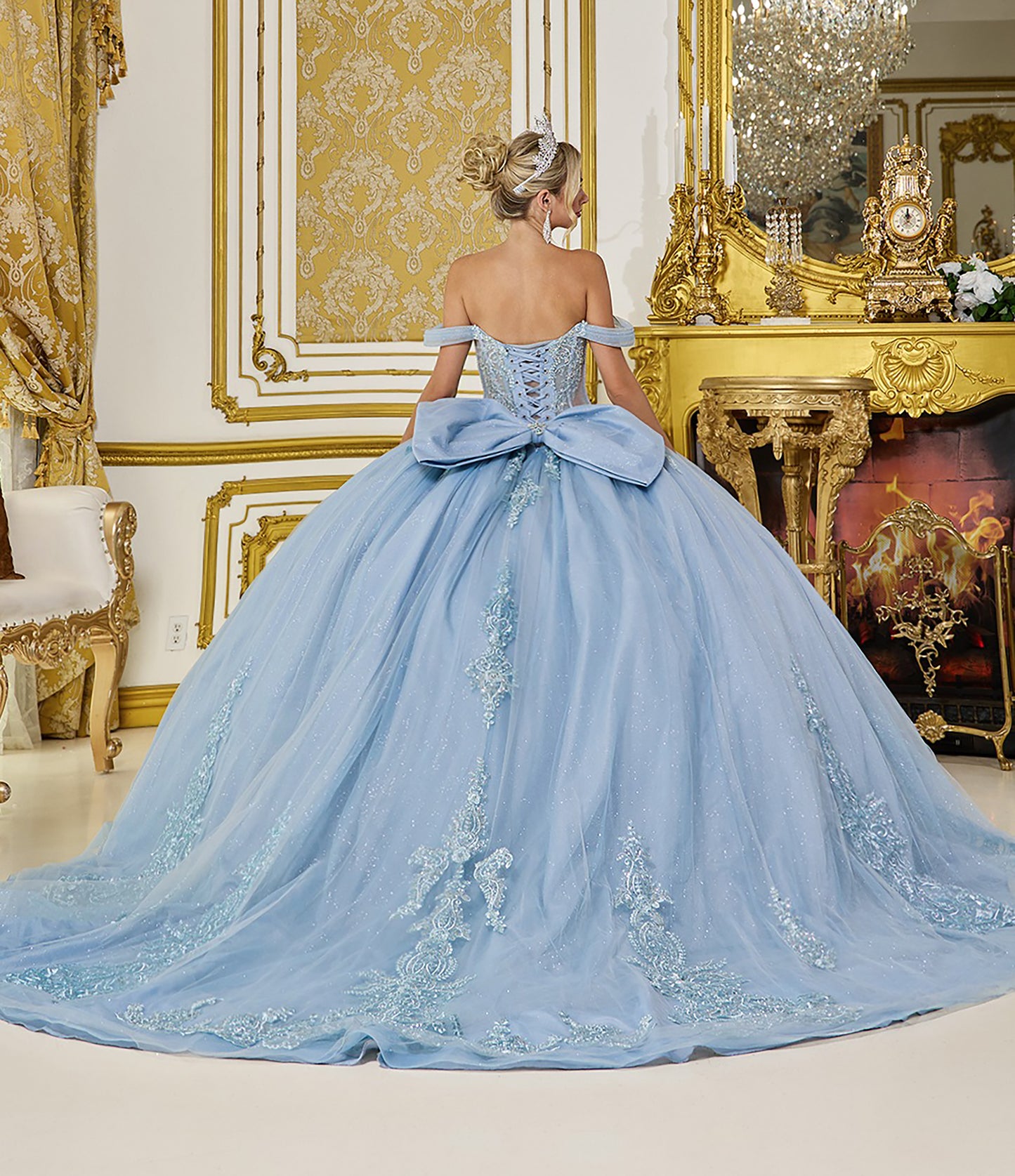 Woman in a light blue gown with a large bow in an ornate room.