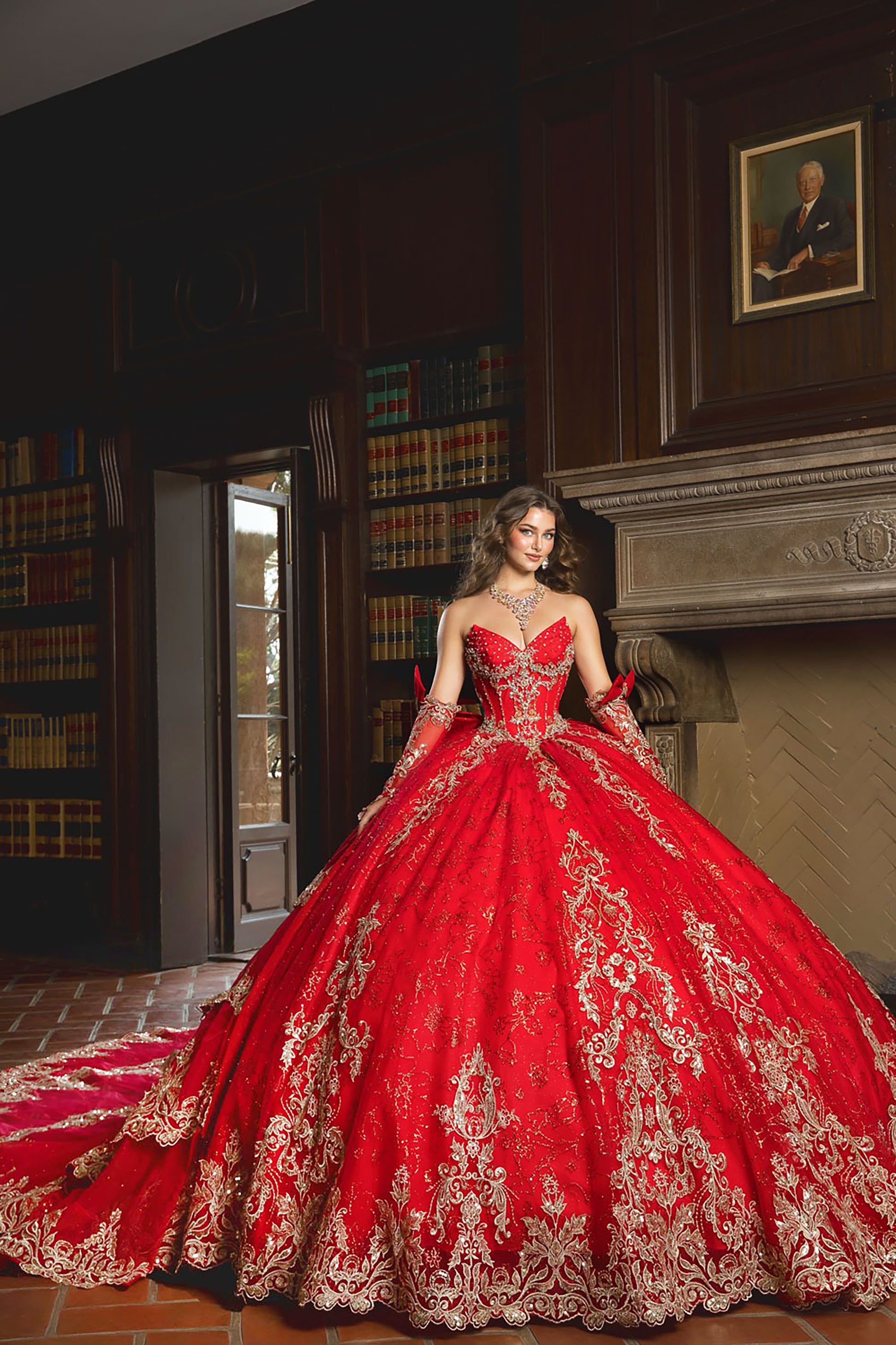 Woman in a red and gold embroidered gown standing in a room with bookshelves and a fireplace.