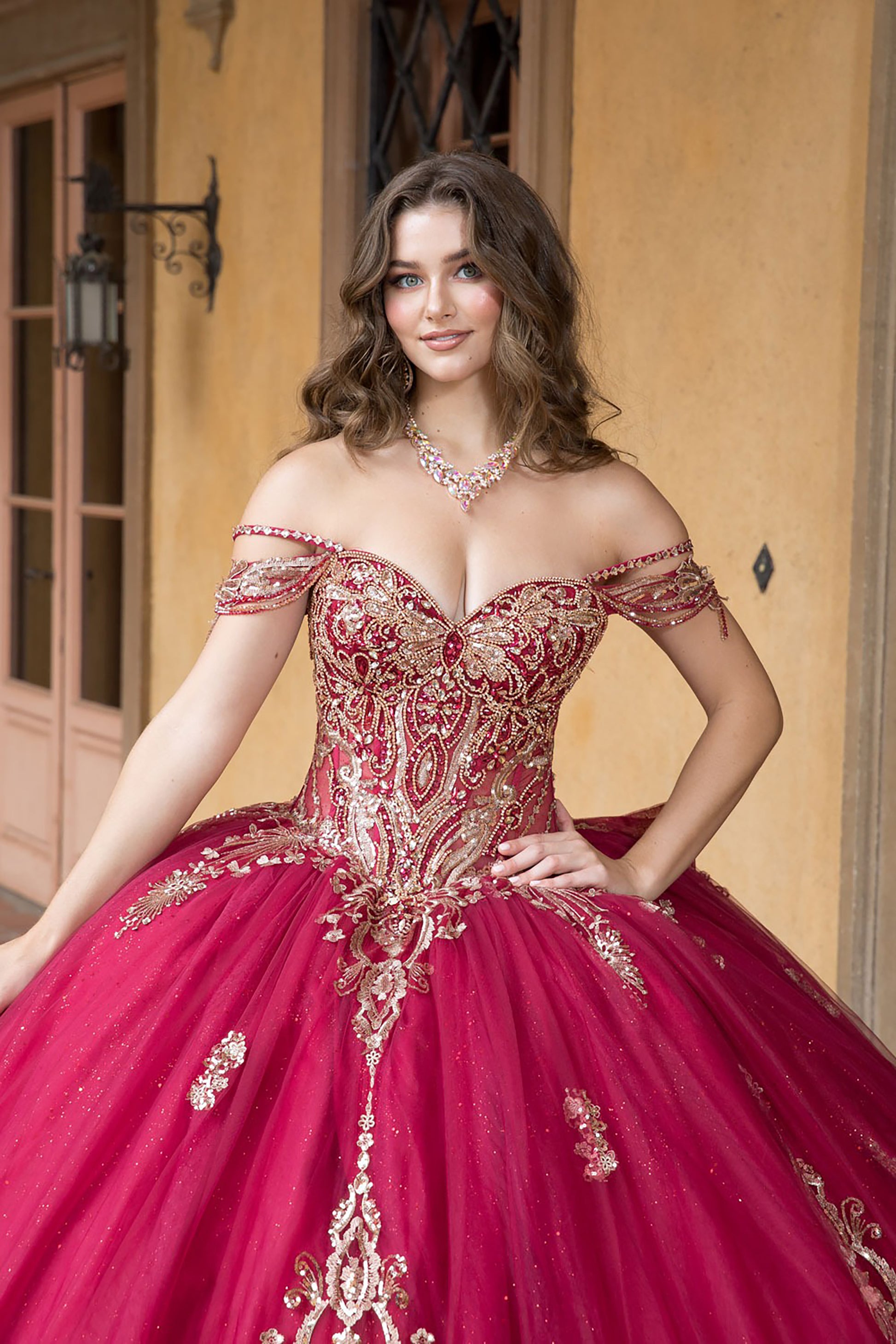 Woman wearing a red and gold off-shoulder gown with intricate detailing.