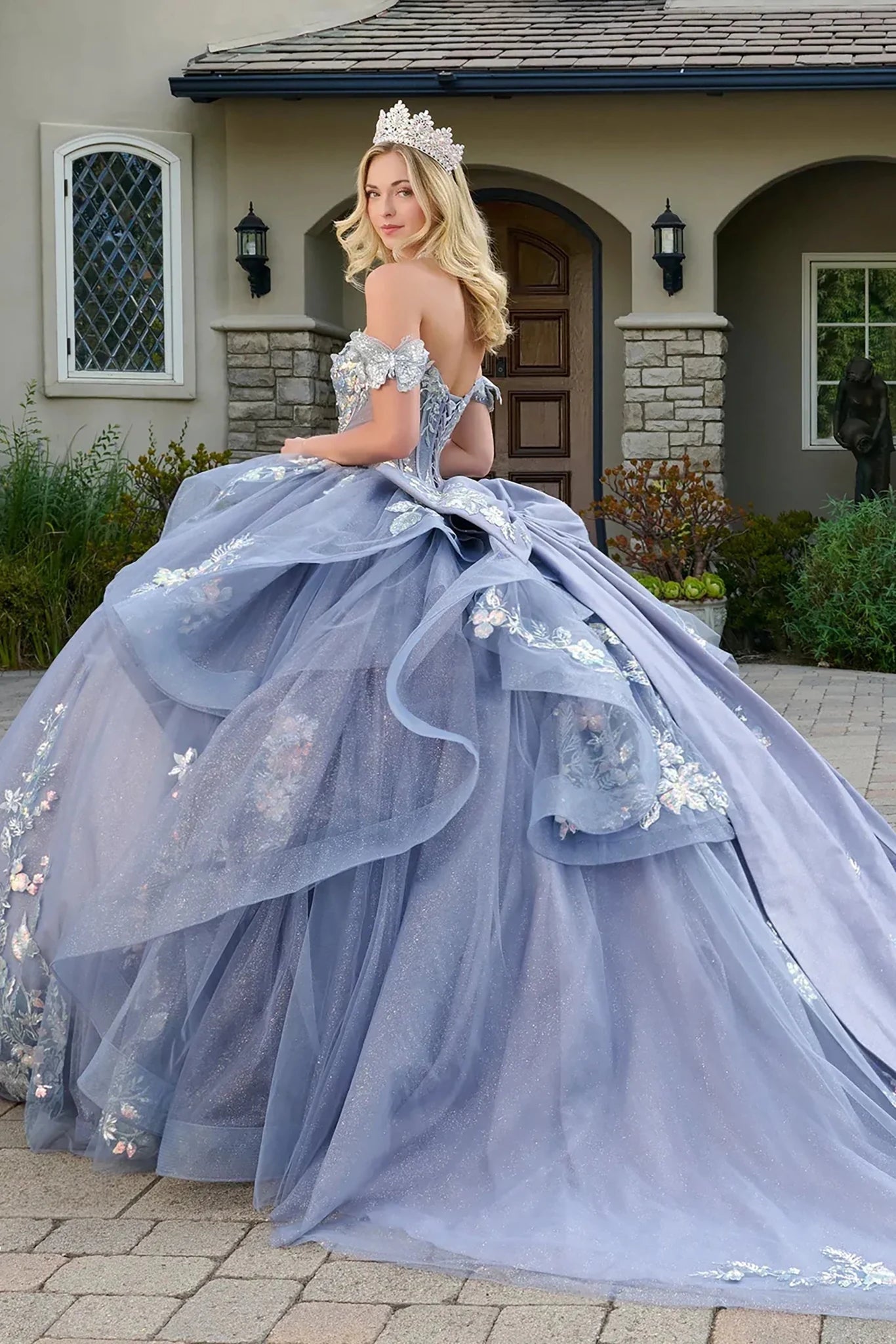 Woman in a blue ball gown with floral details standing in front of a house.