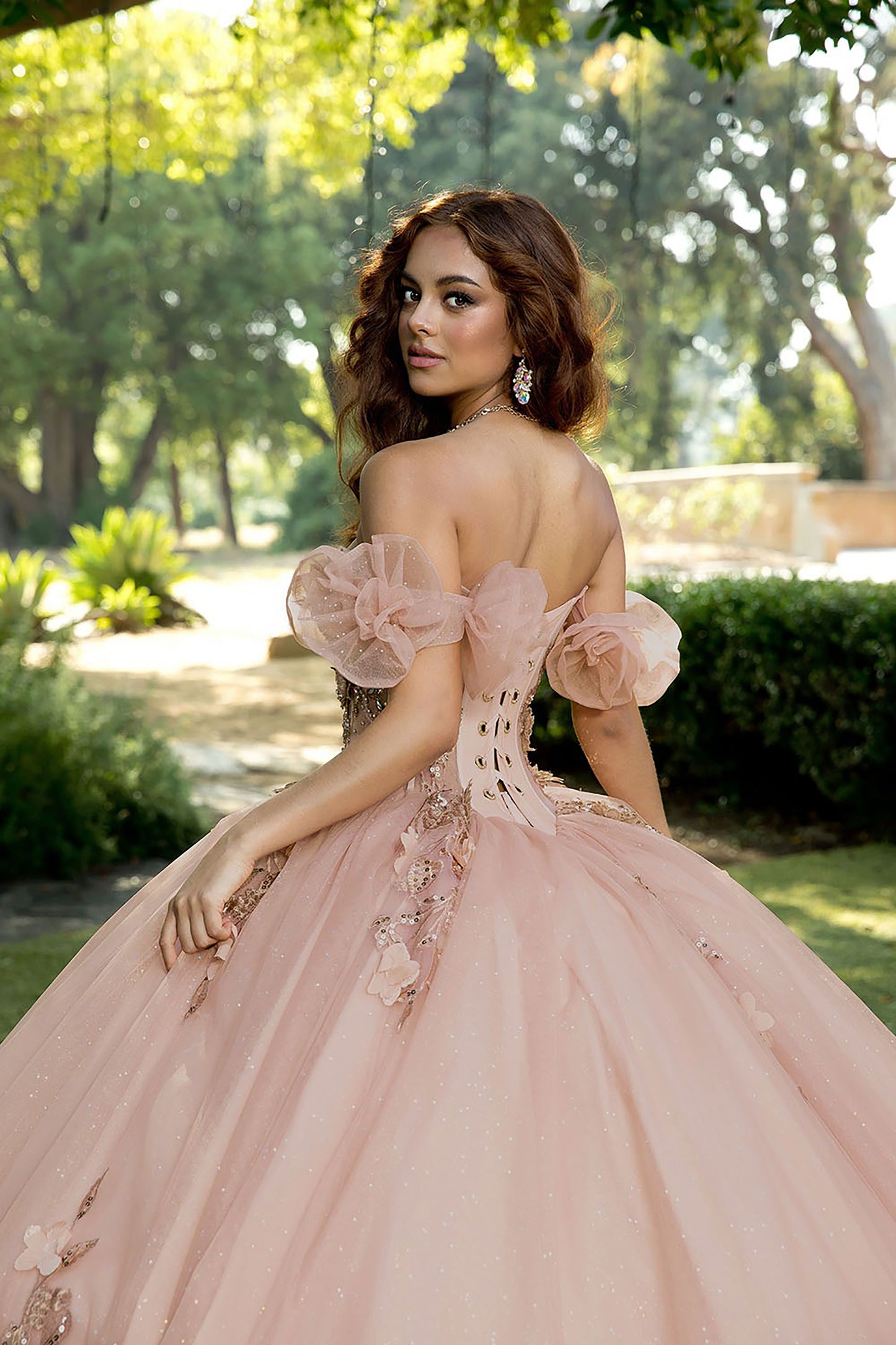 Woman in a pink ball gown with floral details standing outdoors.