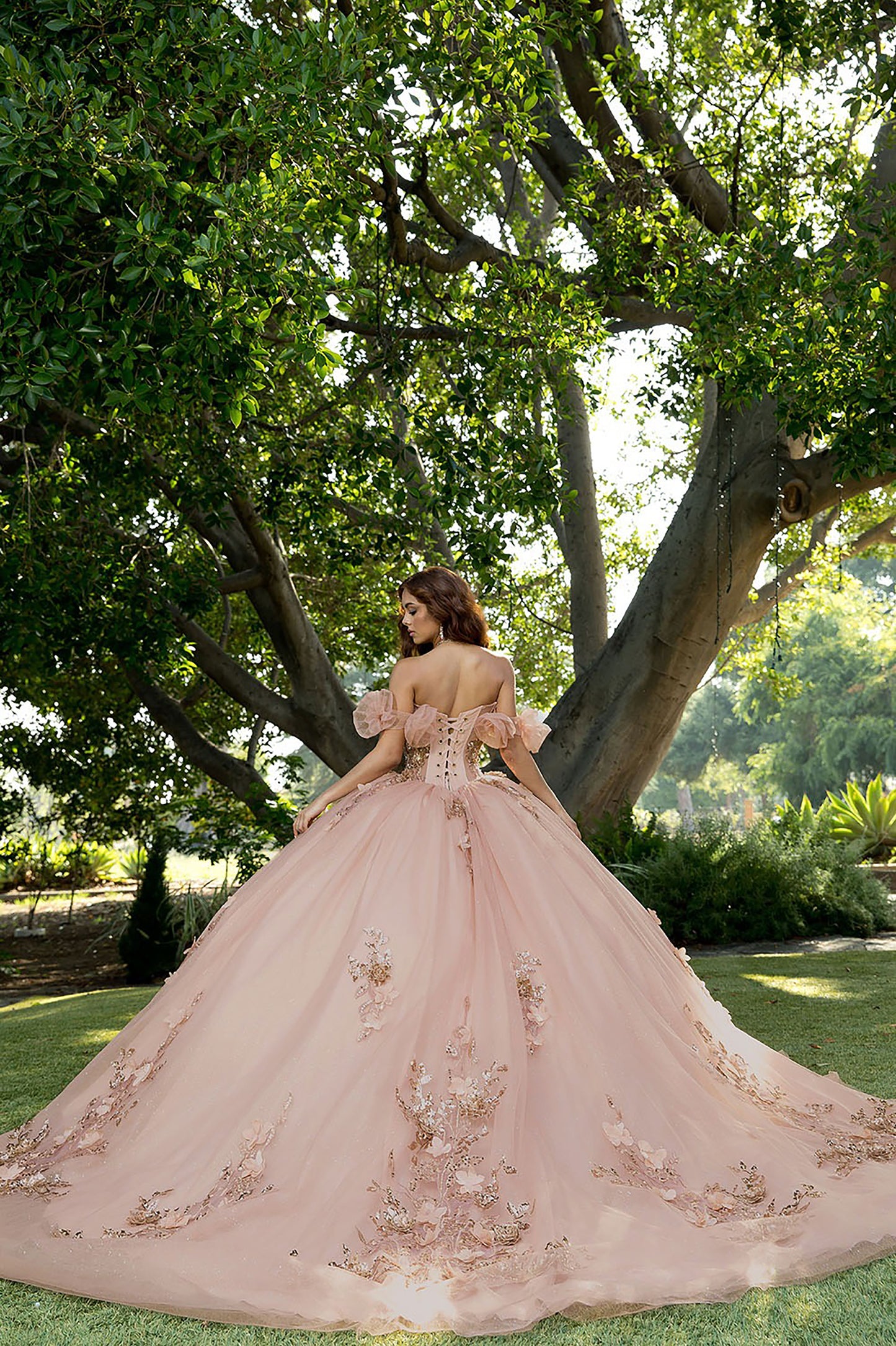 Woman in a pink embroidered gown standing under a tree in a garden