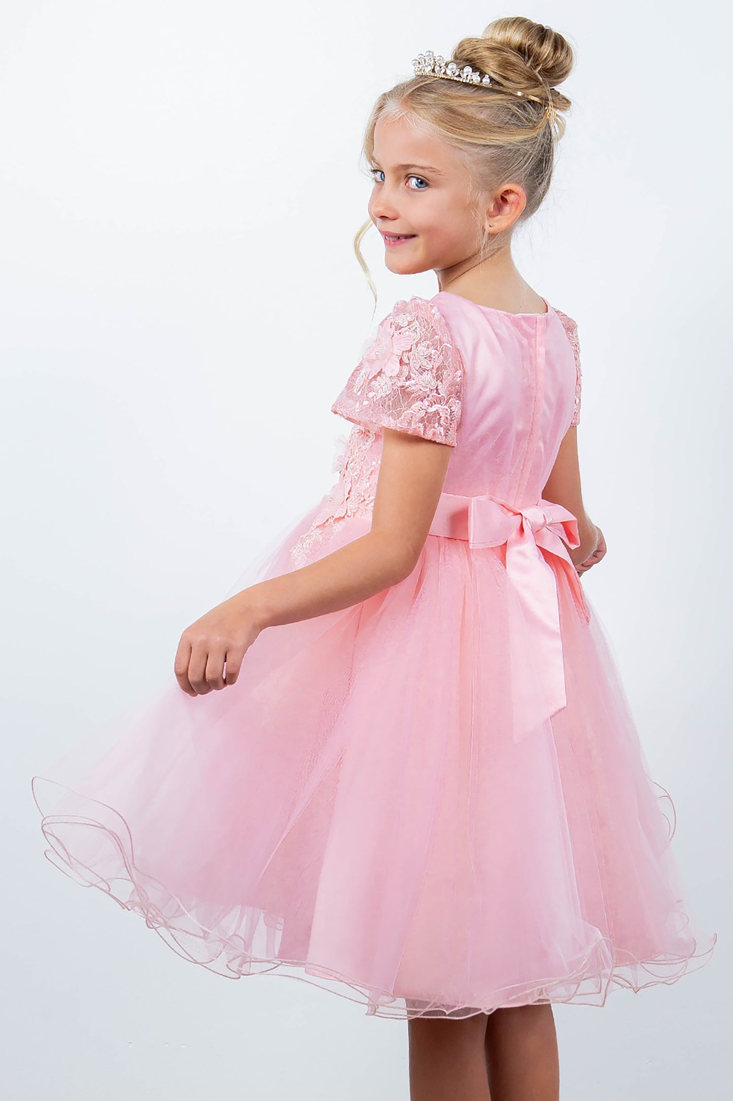 Young girl wearing a pink dress with floral embellishments on a white background