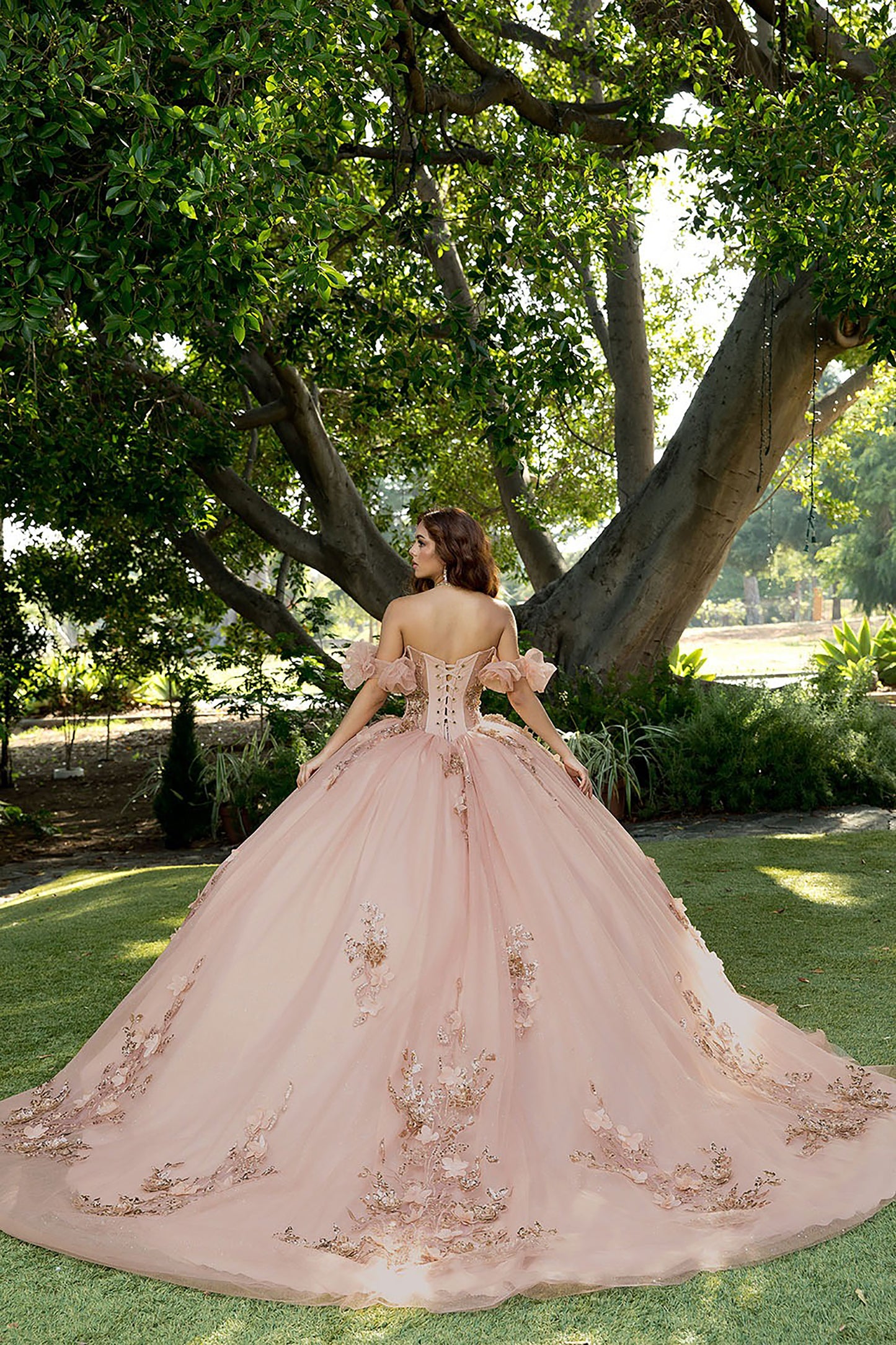 Woman in a pink gown with floral details standing in a garden.