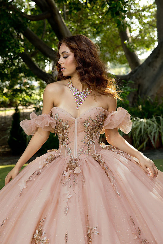 Woman in a pink gown with floral embellishments standing outdoors.